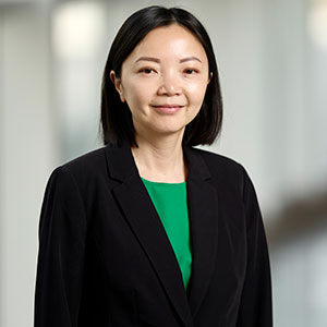 Professional headshot of Tina Fortier, featuring her from the chest up against a softly blurred background. She has dark, shoulder-length hair and is wearing a black blazer over a bright green top.